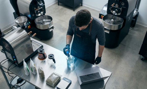 Corporate-style overhead shot of a modern coffee roastery workspace, barista analyzing water quality
